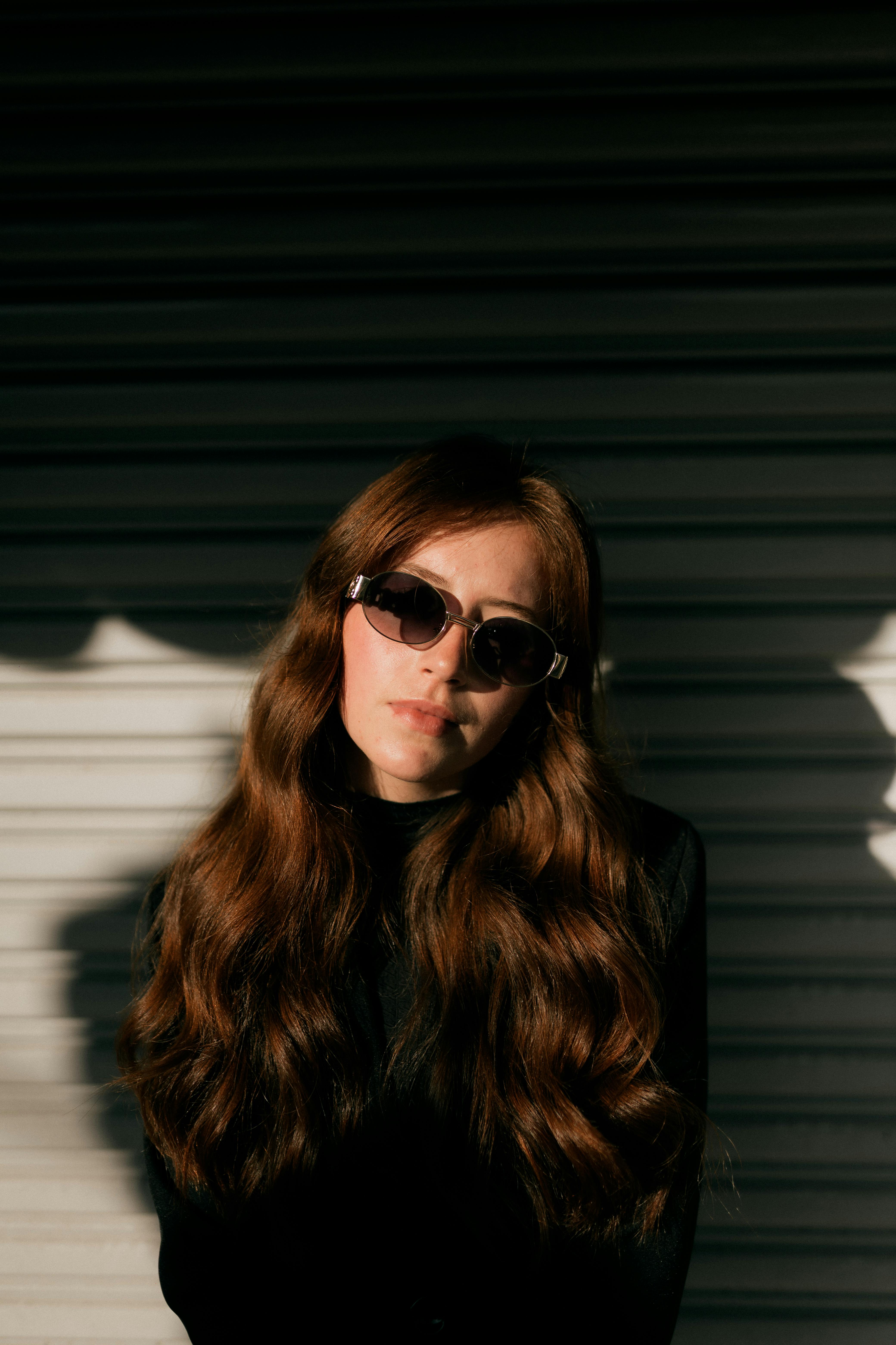 Elegant woman with sunglasses and long hair posing in sunlight. Modern fashion portrait.