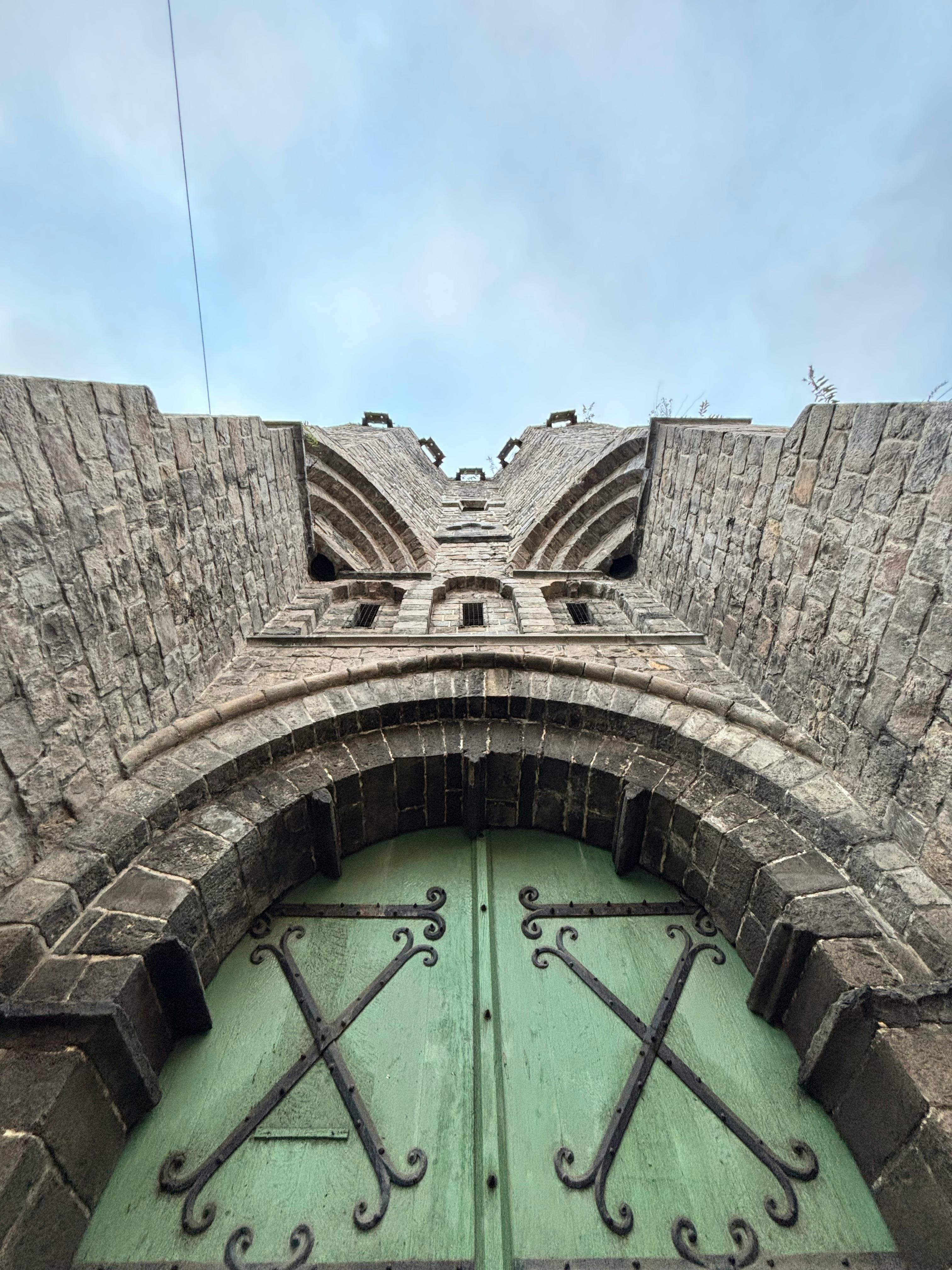 哥特式石头建筑的低角度视图，绿色拱门和天空背景