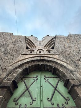 哥特式石头建筑的低角度视图，绿色拱门和天空背景