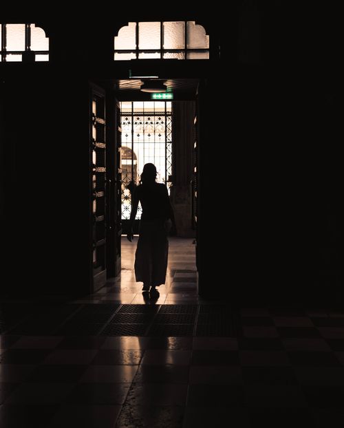 Free A silhouette of a woman walking through a historic hallway with ornate doors, offering a moody ambiance. Stock Photo