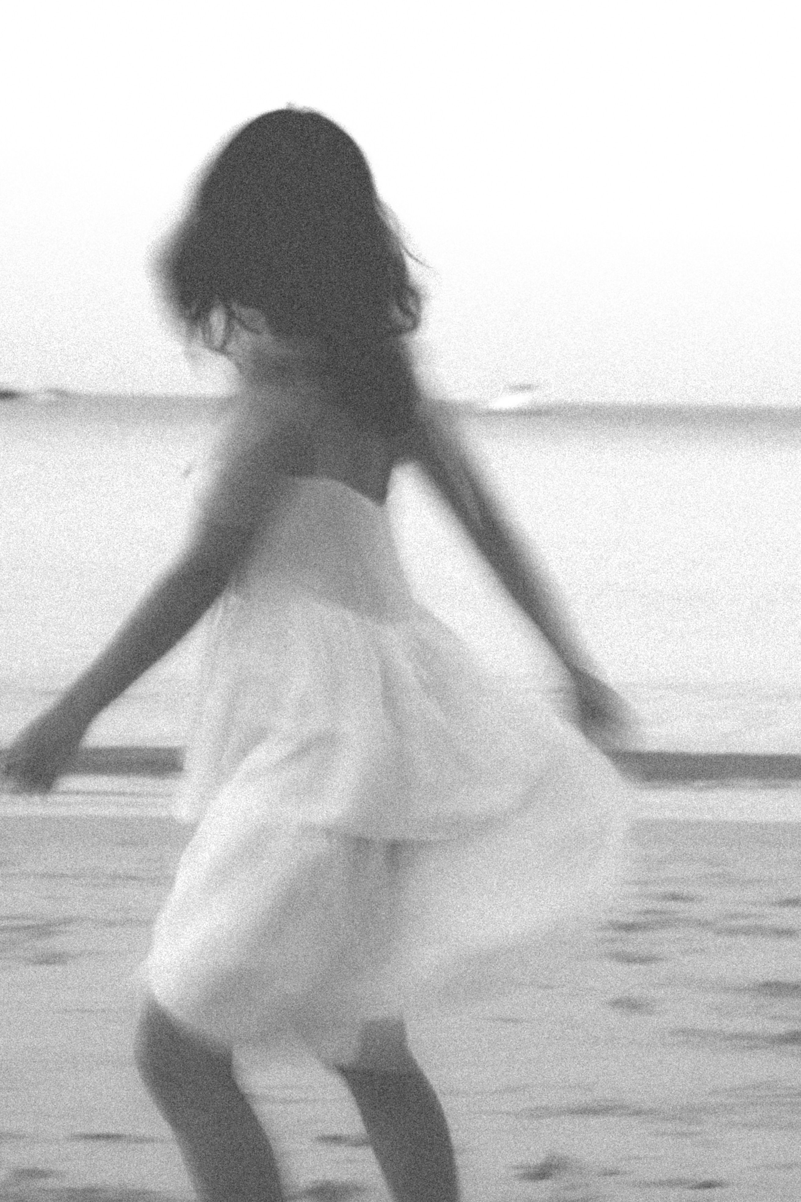Dreamy black and white image of a girl twirling on a beach, capturing movement and emotion.