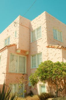 A pastel pink stucco house with white windows under a clear blue sky.