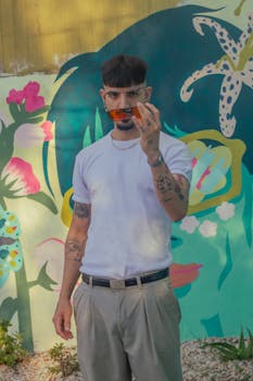 Trendy man with tattoos holds sunglasses in front of a colorful mural. Captured outdoors in Argentina.