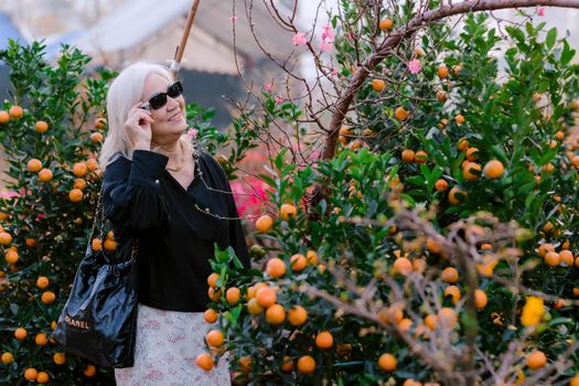 Stylish senior woman in sunglasses appreciating vibrant citrus garden.