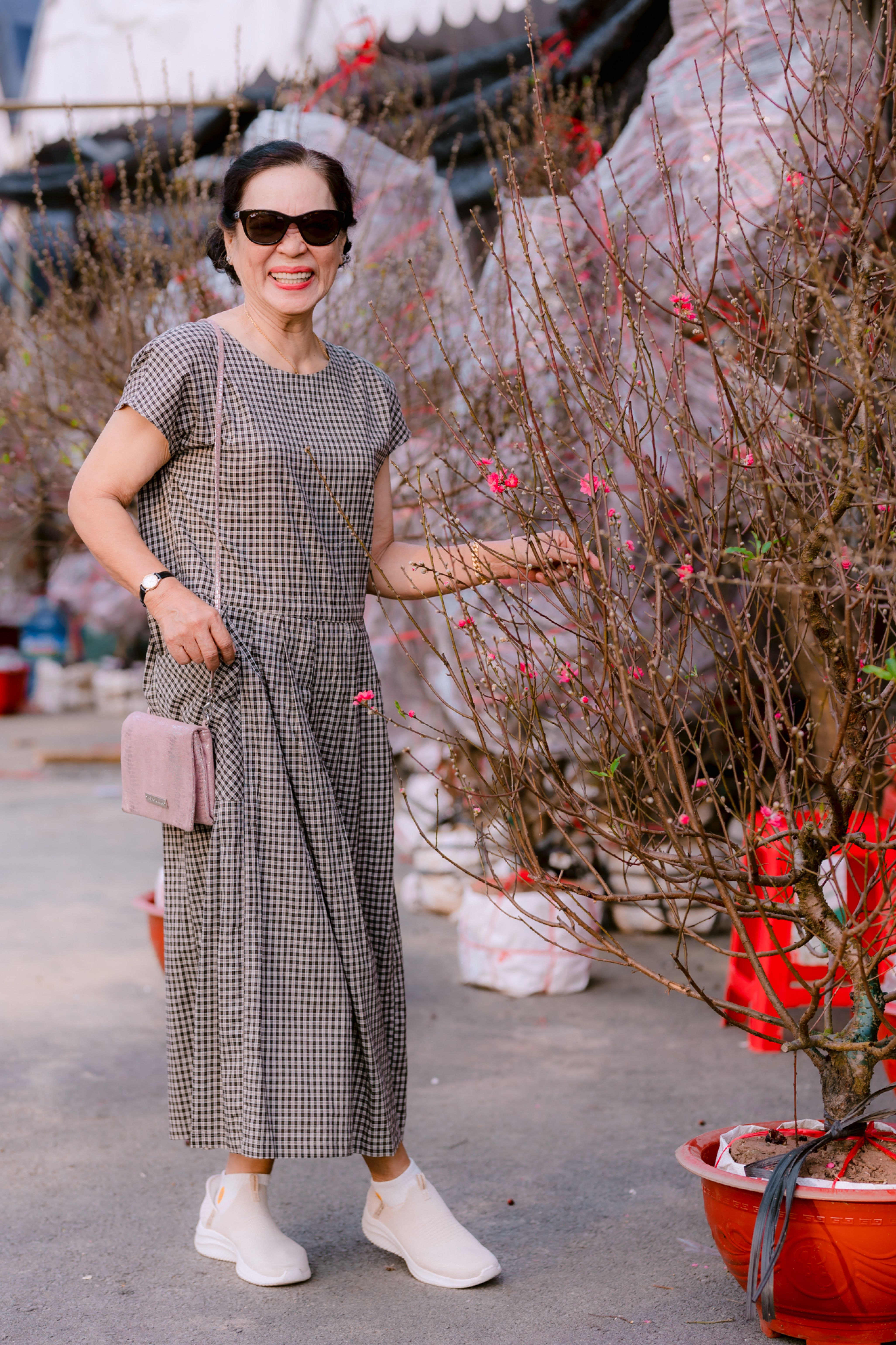 Stylish woman in sunglasses posing with blooming cherry trees outdoors.
