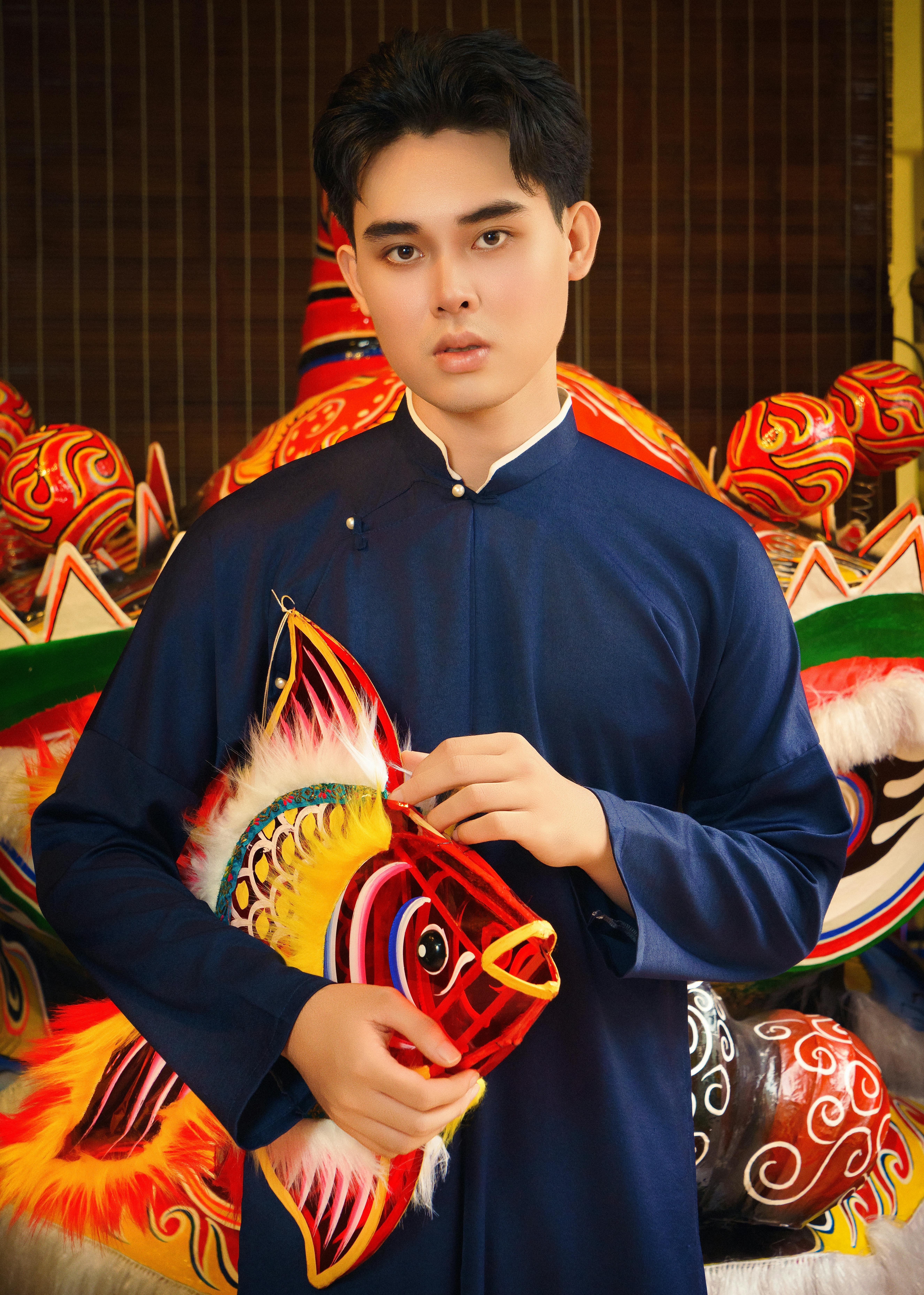 Young man in traditional attire holding a colorful fish lantern at a cultural festival in Vietnam.