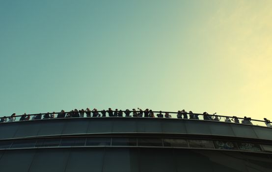 Dramatic silhouettes of people enjoying a glass walkway view in Hong Kong against the sunset.