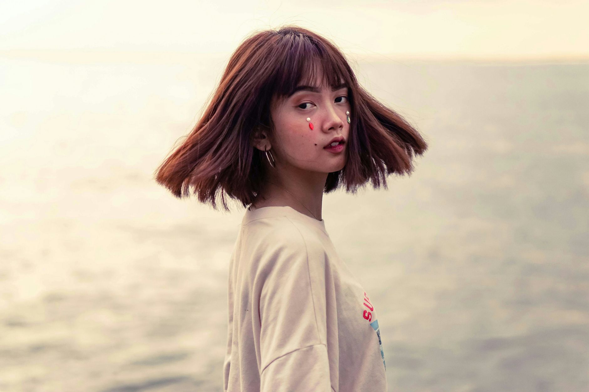 A young woman with short hair poses by the sea with thoughtful expression.