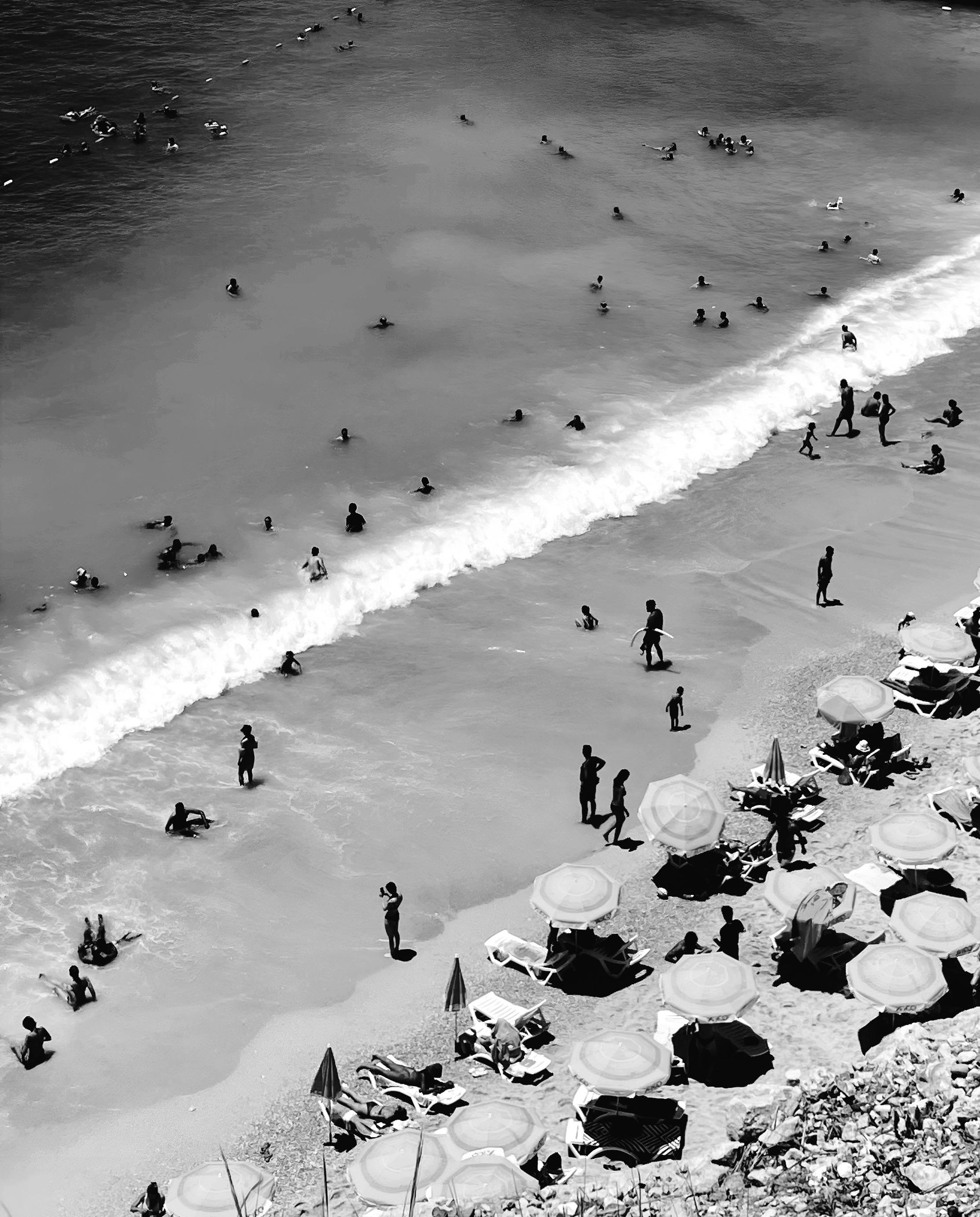 鸟瞰拥挤的海滩，看到有海浪、雨伞和黑白色的游泳者