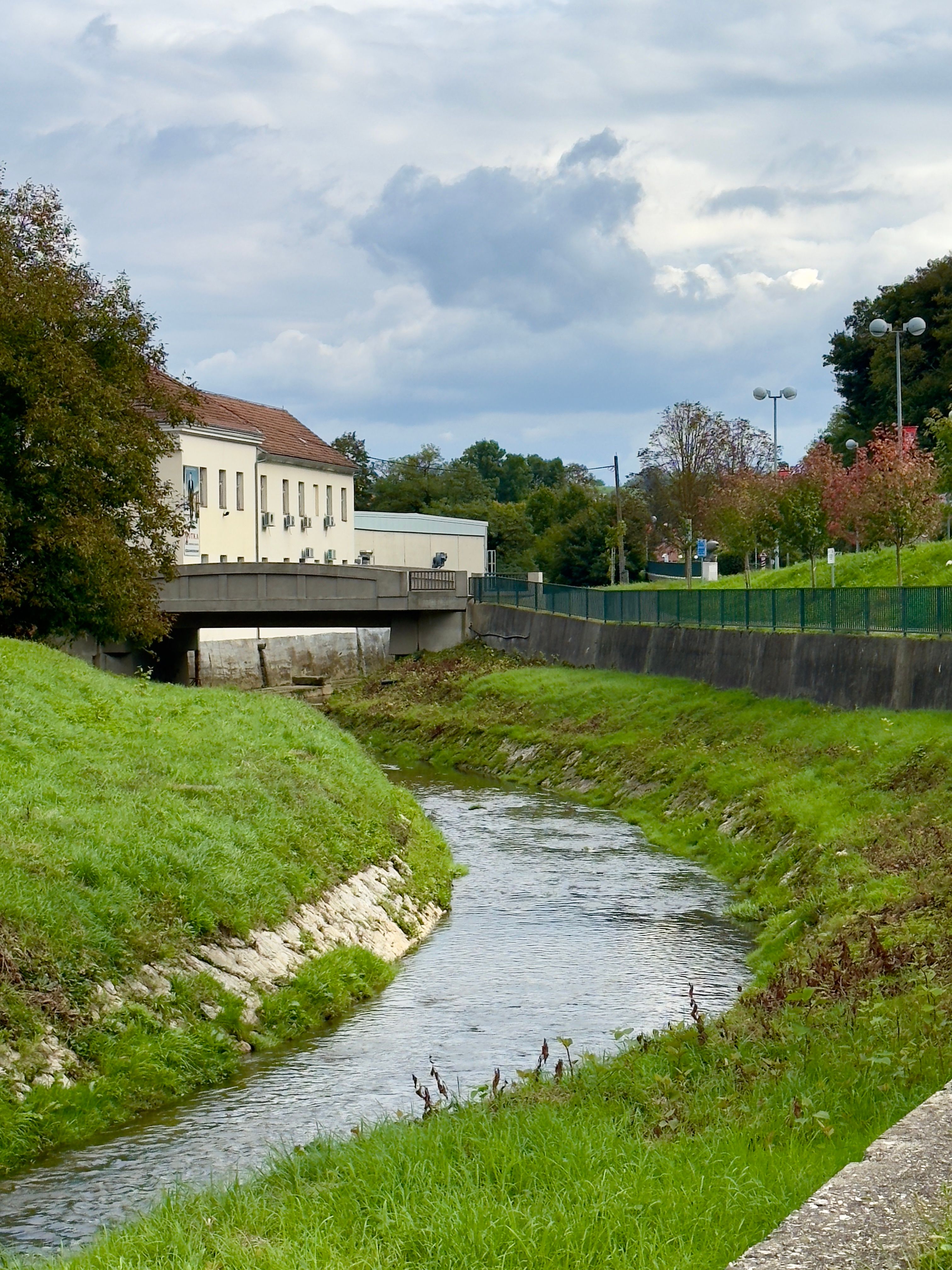 Stream flowing through green grass with a bridge and building in Krapina, Croatia