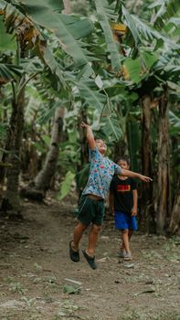Two children joyfully play under lush banana trees, capturing a moment of carefree happiness.
