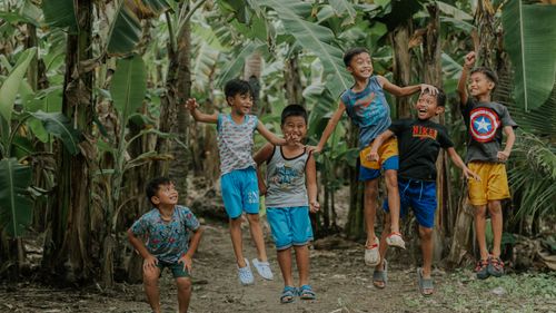 Free Group of joyful children playing and jumping between rows of banana trees outdoors. Stock Photo