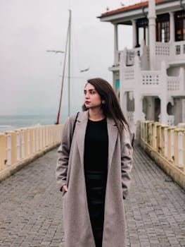 Stylish woman in coat on a pier with ocean backdrop. Cloudy day mood.