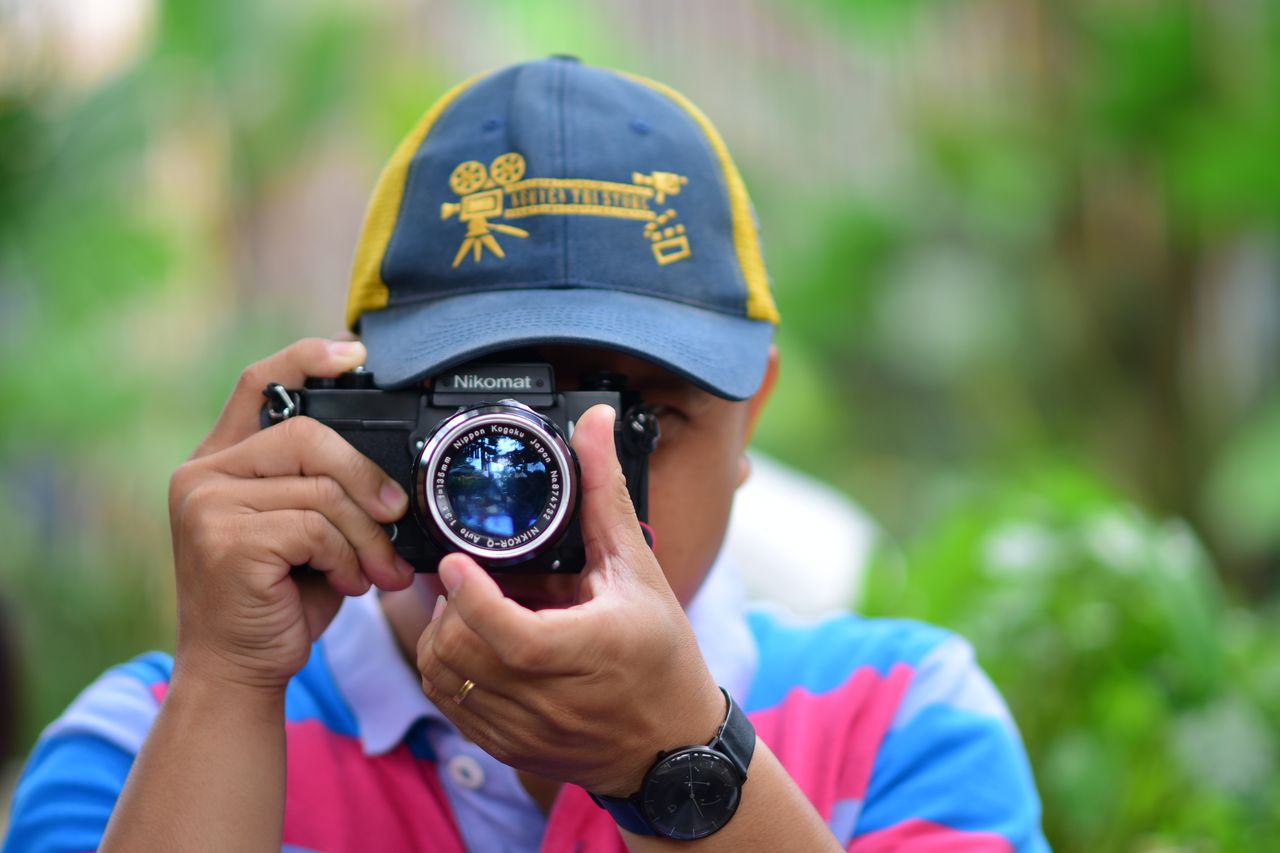 a person wearing a cap takes a photo using a vintage camera outdoors