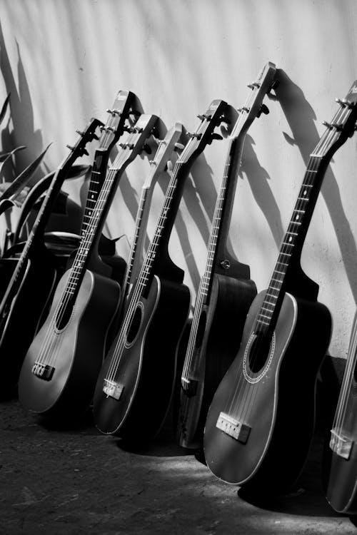 Free Black and white of many acoustic guitars leaned on wall on street on sunny day Stock Photo