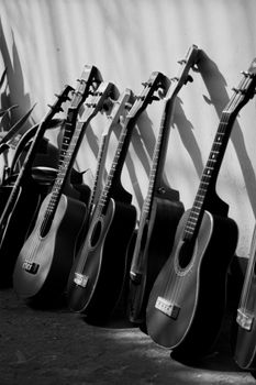 Black and white of many acoustic guitars leaned on wall on street on sunny day