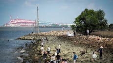 人们在晴朗的天空下探索繁忙的集装箱港口附近的岩石海岸