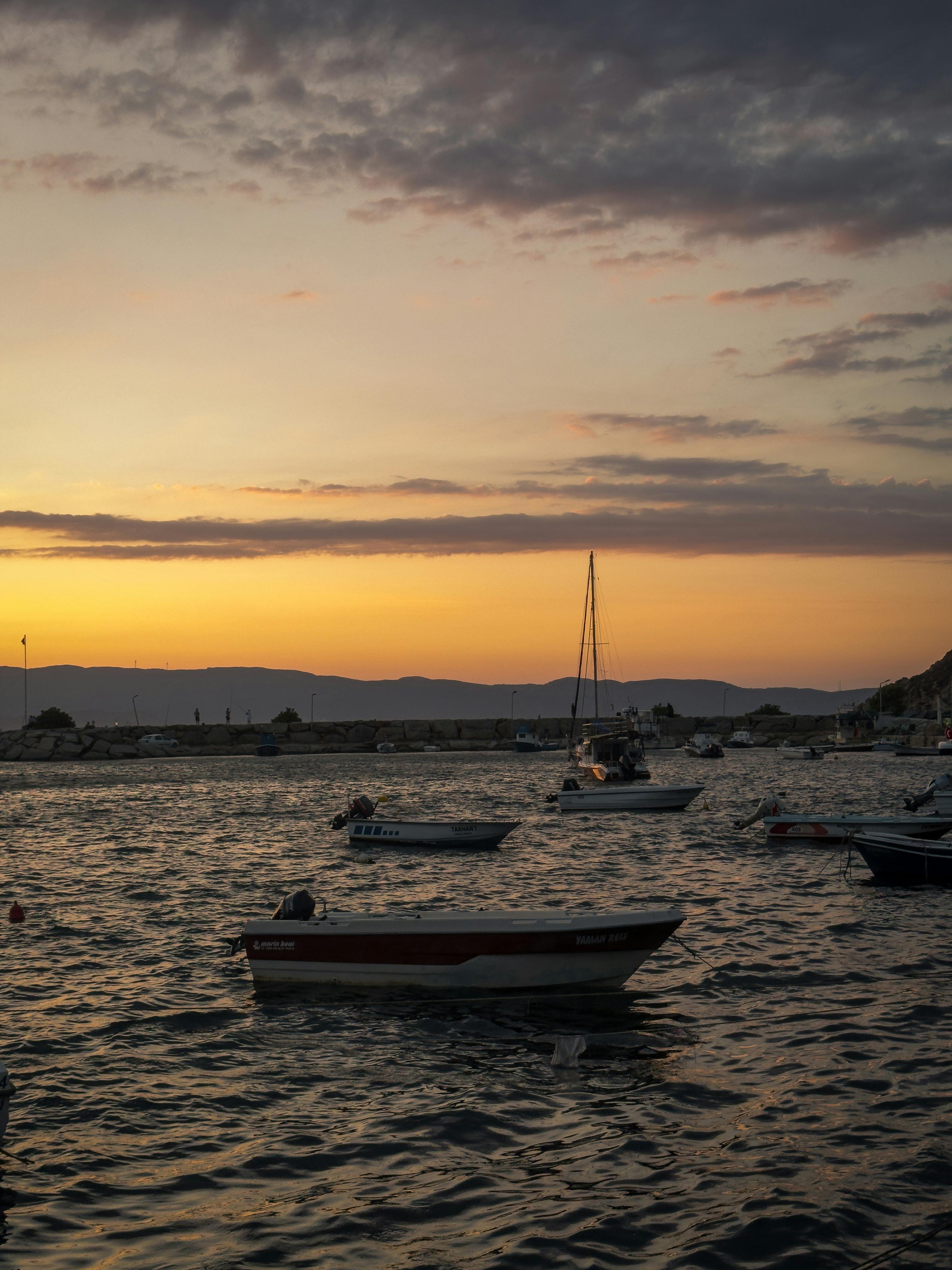 日落时分，船只在宁静的港口中漂浮，而地平线上山脉若隐若现
