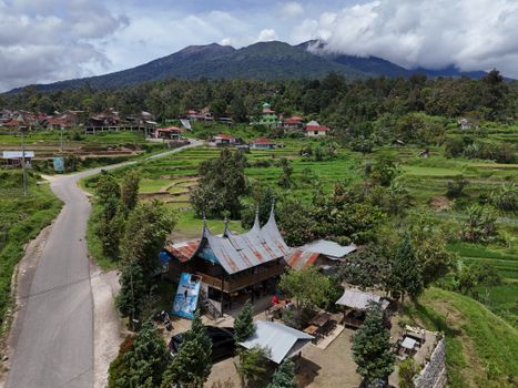 A beautiful aerial shot of a Minangkabau village with lush green rice fields and mountains in West Sumatra, Indonesia.