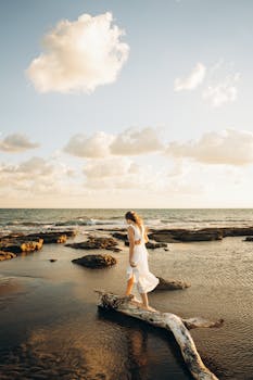 Woman in white dress walking along a tranquil beach in Antalya at sunset, reflecting calm and serenity.