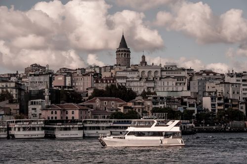 Free A scenic view of Istanbul's Galata Tower with boats on the Bosphorus, captured under dramatic skies. Stock Photo