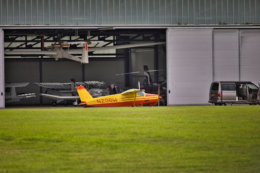 Yellow airplane parked near an open hangar on a sunny day. Modern aviation setting.