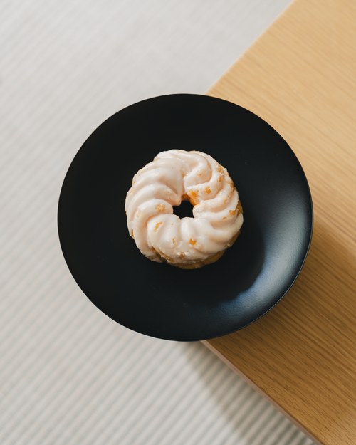 Free Close-up of a frosted doughnut on a sleek black plate, perfect for food photography. Stock Photo