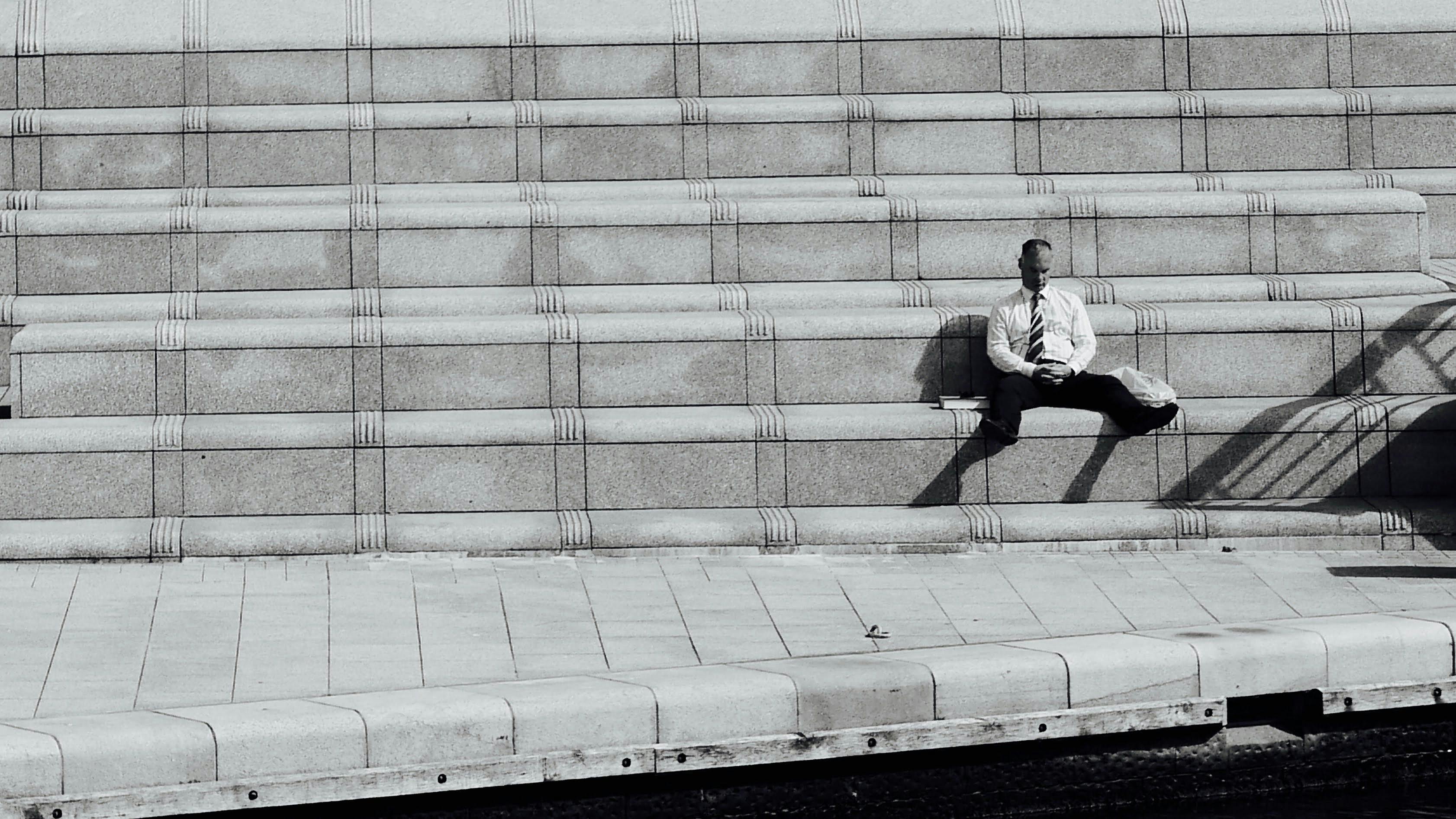 Free A lone man in formal attire sitting on city steps, surrounded by architectural symmetry. Stock Photo