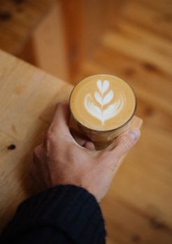 A close-up of a hand holding a latte with beautiful latte art in a cozy setting.