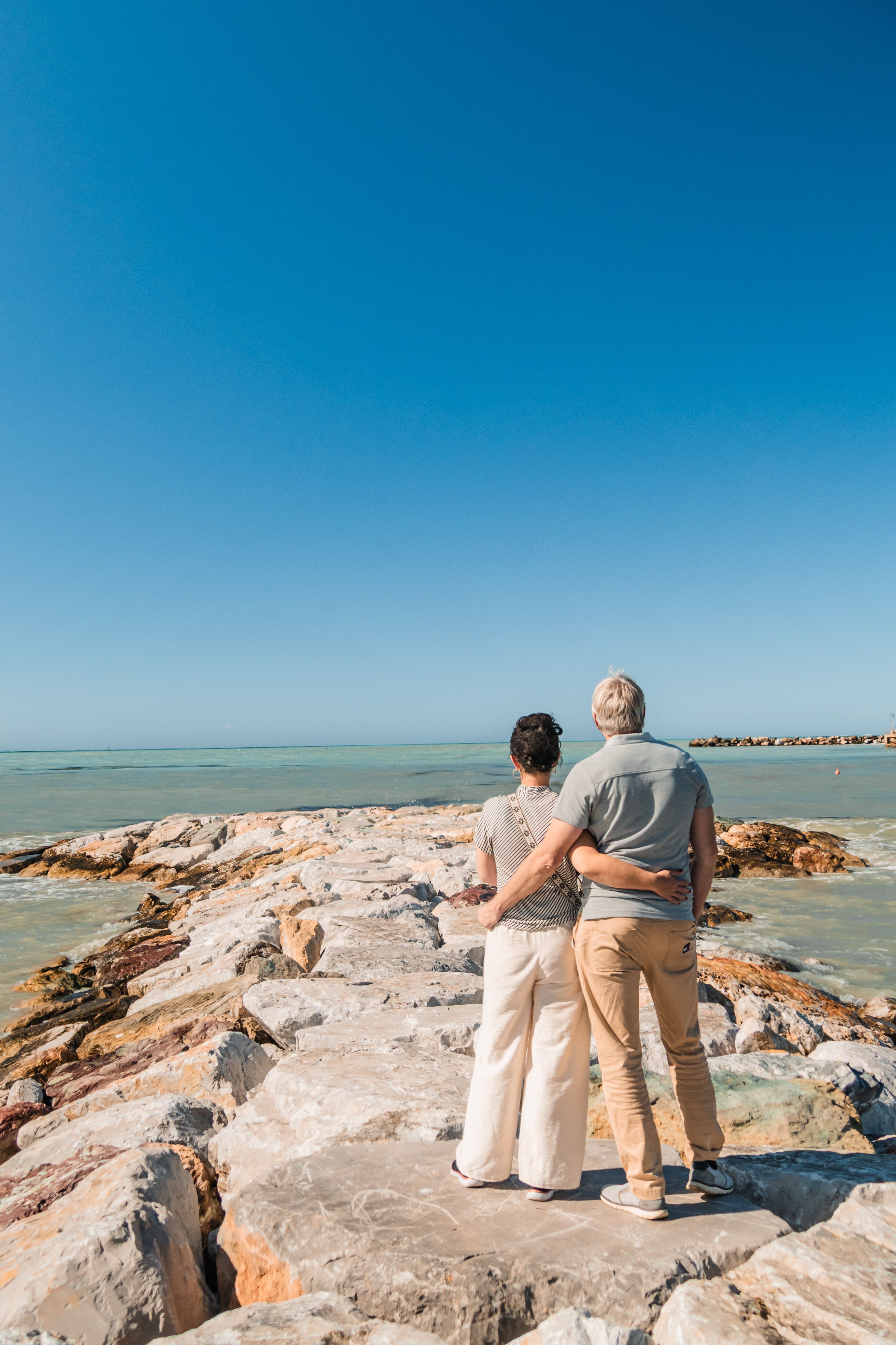A couple stands on a rocky pier overlooking the sea in Vada, Tuscany, enjoying a bright summer day.