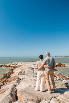 A couple stands on a rocky pier overlooking the sea in Vada, Tuscany, enjoying a bright summer day.