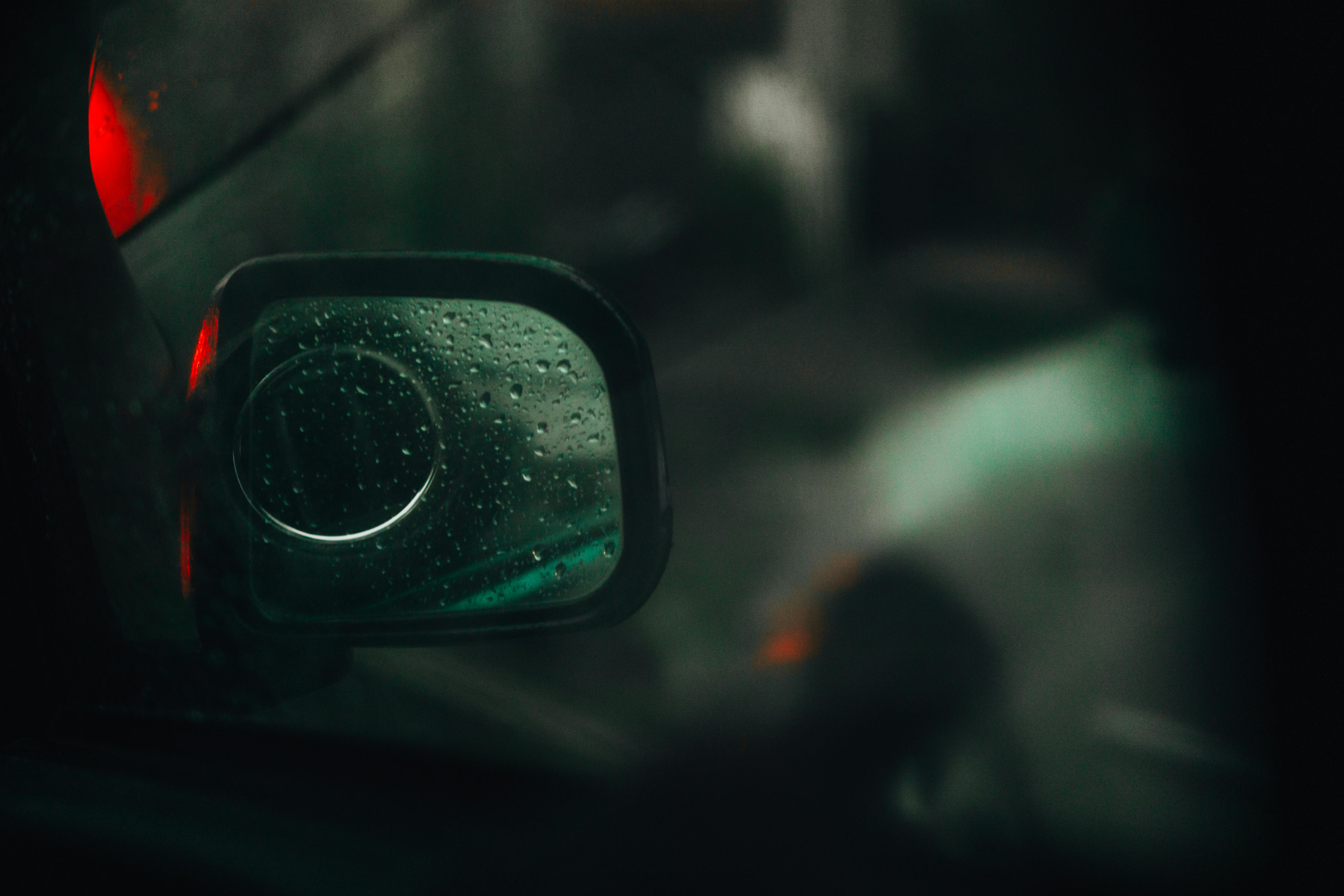 Gratis Primo piano dello specchietto laterale di un'auto con gocce di pioggia di notte, che mettono in risalto la superficie riflettente e il fanale posteriore rosso. Foto a disposizione