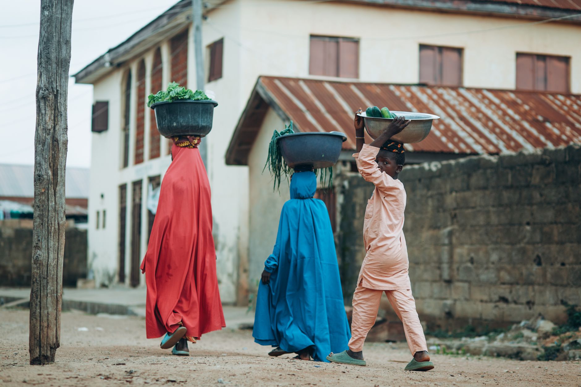 Vibrant street scene in Kaduna, Nigeria, capturing women in colorful attire carrying goods on their heads.