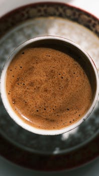 Aromatic coffee with frothy top viewed from above, set in a decorative cup and saucer.