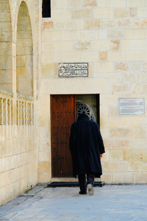 Free Person in dark coat entering a historic stone building through wooden door. Stock Photo