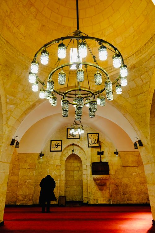 Free Luxurious chandelier hangs in a historic mosque with ornate architecture and warm lighting. Stock Photo