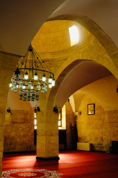 Free Warmly lit interior of a historical mosque featuring arches and a distinctive chandelier. Stock Photo