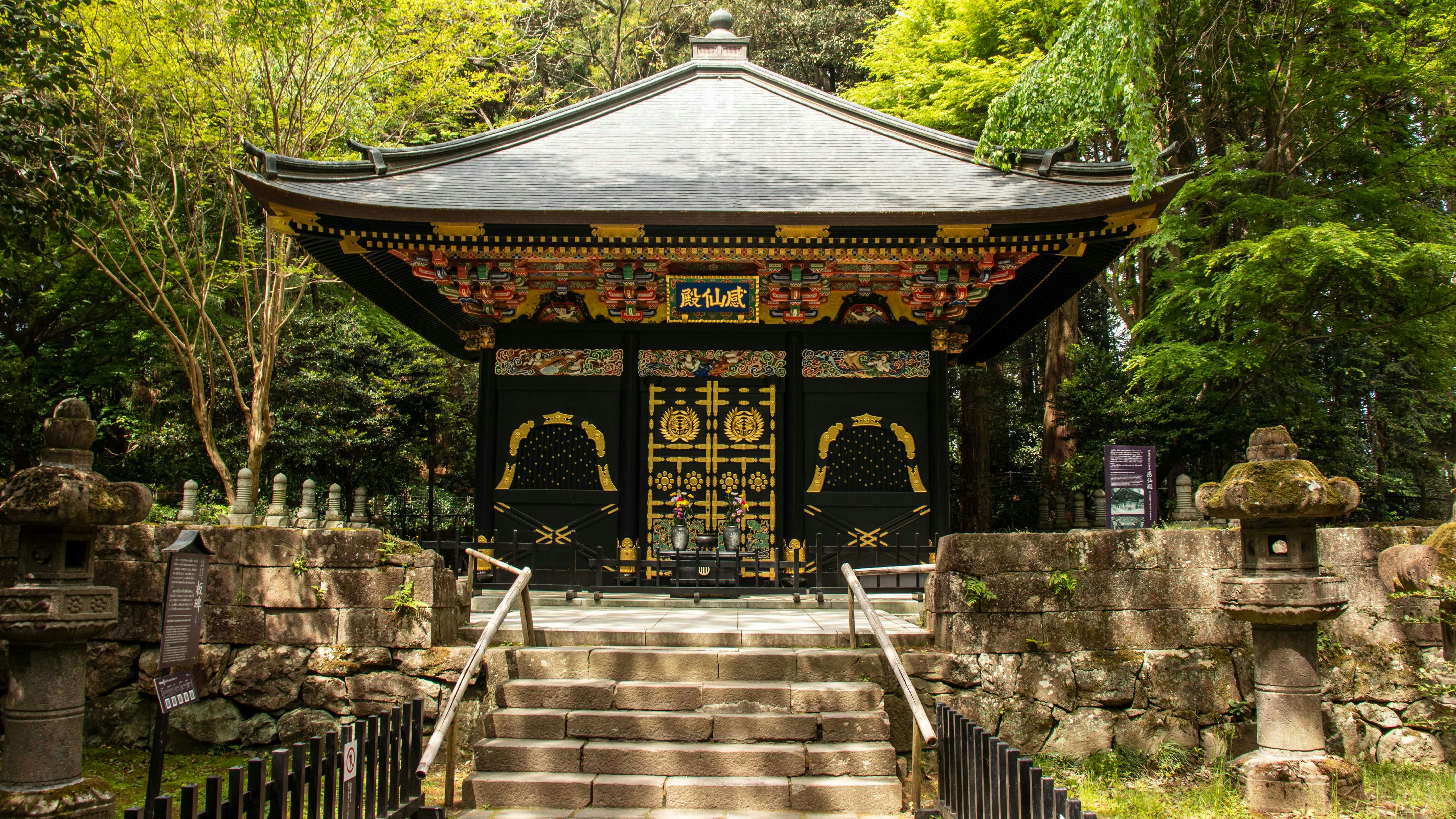 Traditional Japanese temple surrounded by green forest and stone lanterns.
