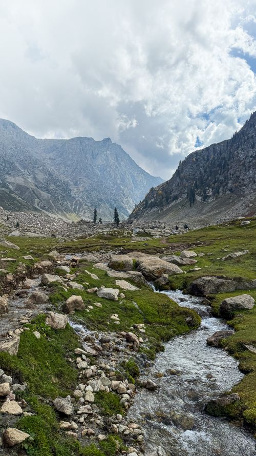 Free Serene mountain view in Hindukush, Pakistan featuring lush greenery and a flowing stream under a dramatic cloudy sky. Stock Photo