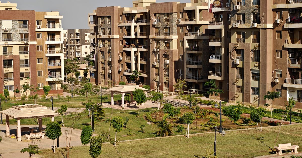 Aerial view of a modern apartment complex surrounded by green gardens under clear skies.