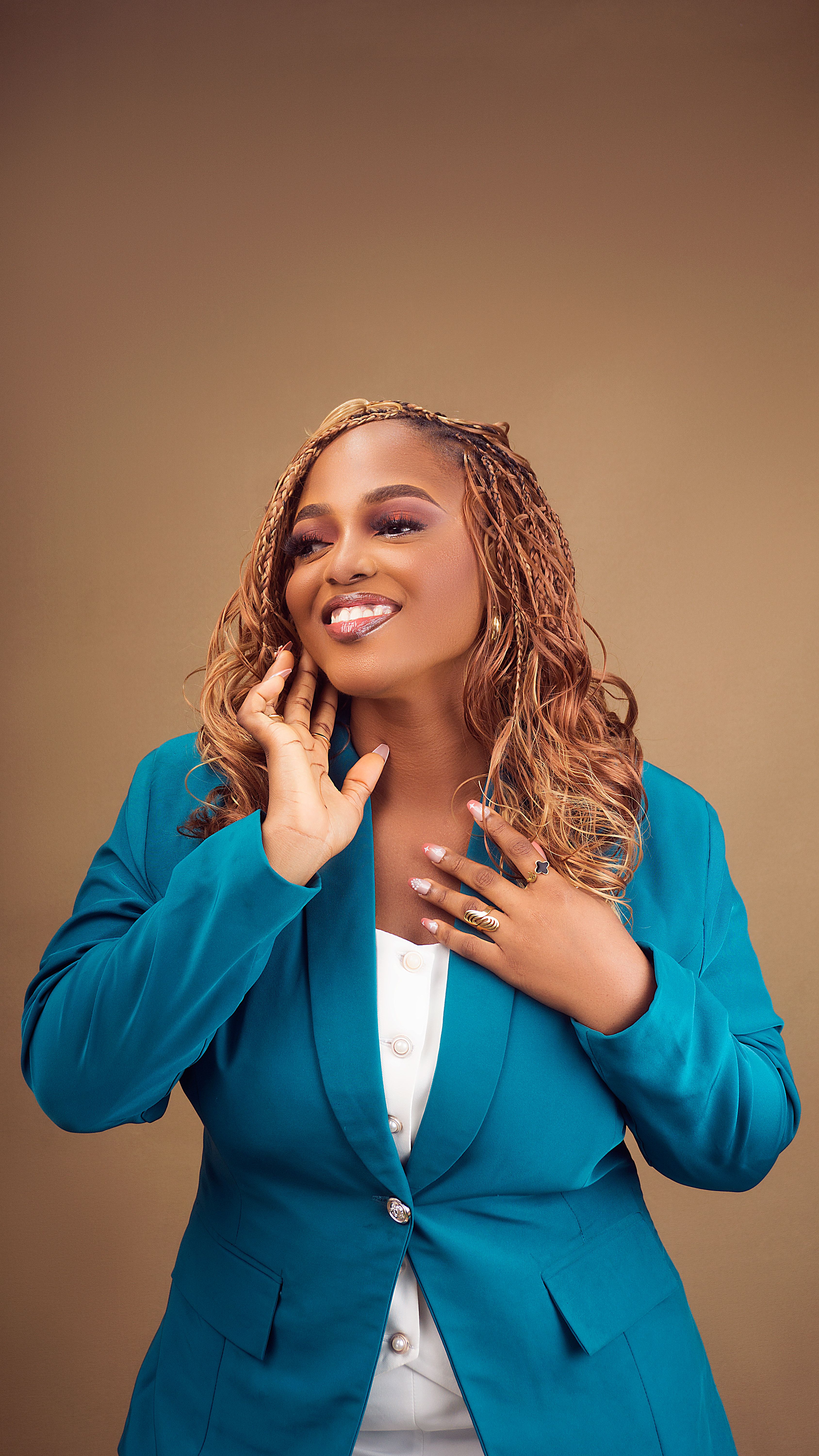 Portrait of a confident woman in a teal blazer posing against a beige background, expressing joy and style.