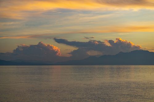 Free A tranquil sunset over the ocean with clouds and a distant mountain range. Stock Photo