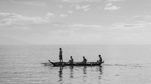 Free Four individuals on a traditional boat against a calm seascape in black and white. Stock Photo