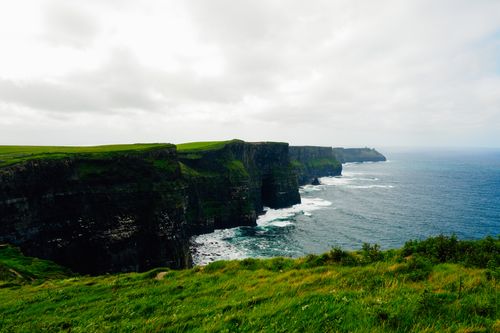 Free A scenic view of the Cliffs of Moher, Ireland, with lush green cliffs and a vast ocean. Stock Photo