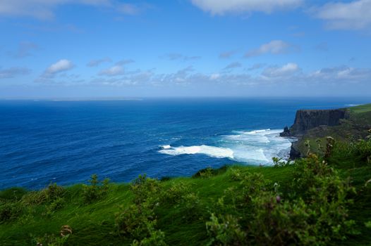 Beautiful view of the Cliffs of Moher with waves crashing against the rocks under a clear blue sky.
