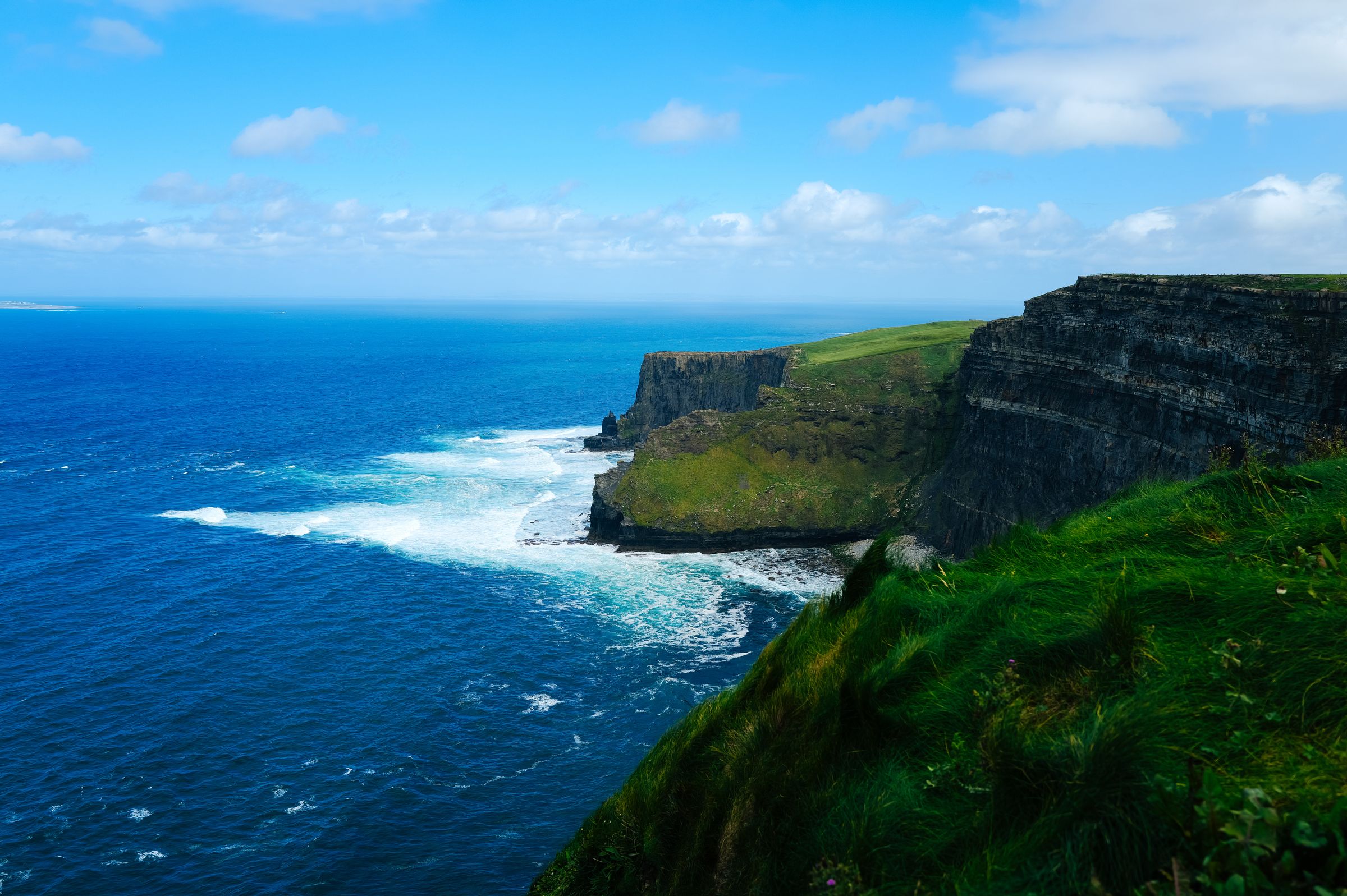 View of the Cliffs of Moher with expansive ocean and greenery under a bright sky
