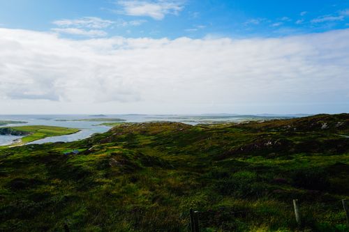 Free Expansive green hills overlooking the ocean under a partly cloudy sky. Stock Photo