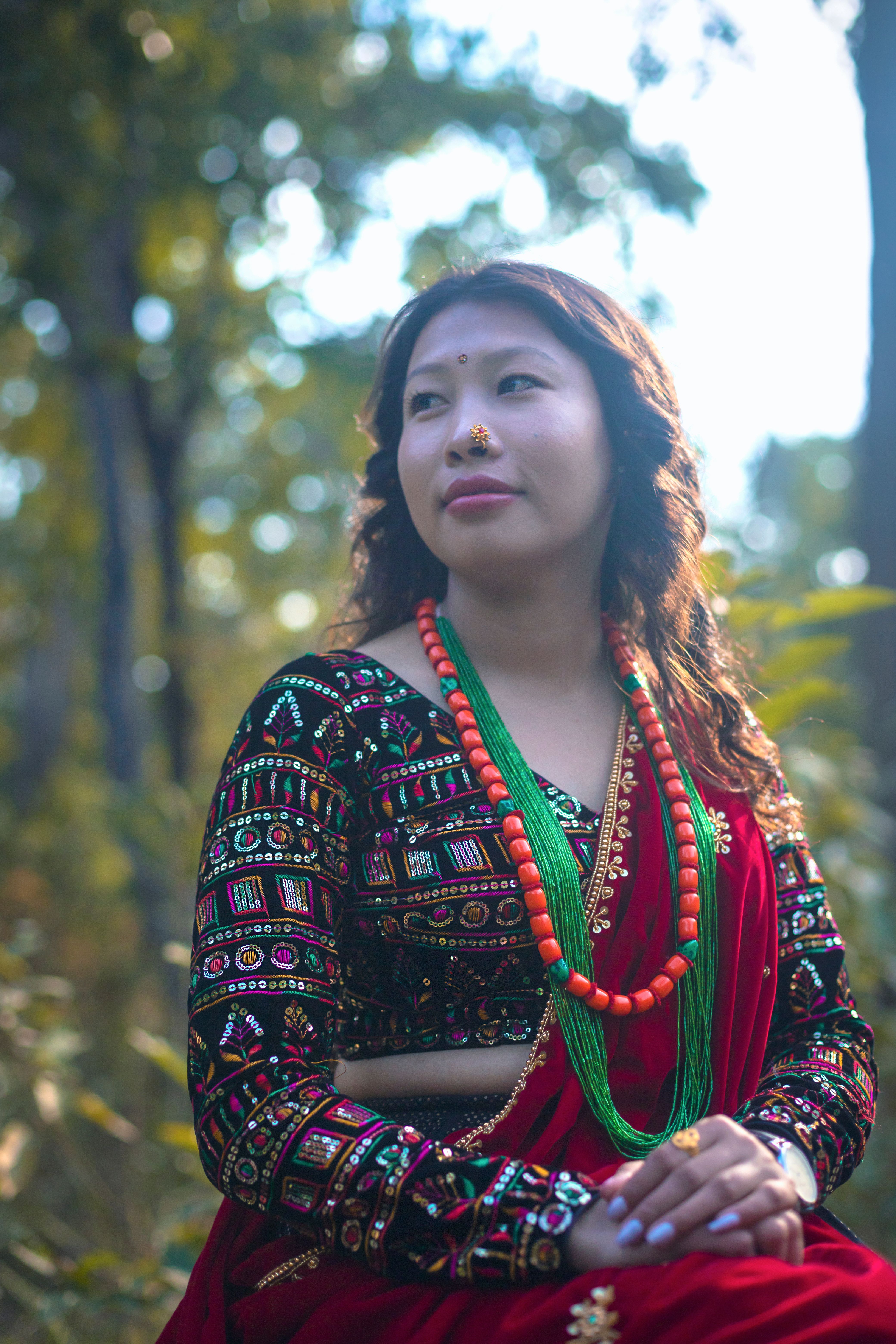 A Magar woman in traditional clothing and jewelry in an outdoor Nepalese setting.