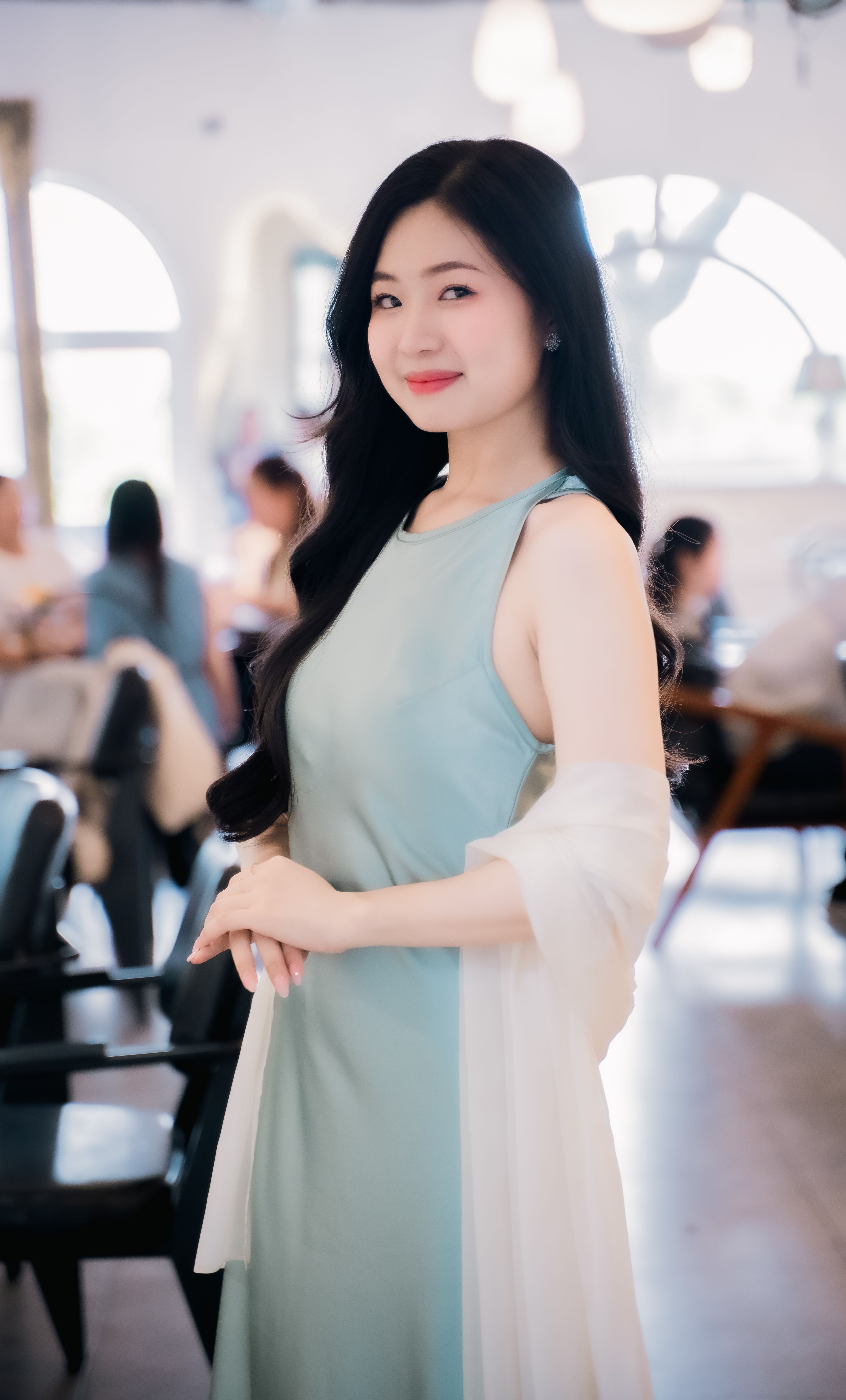 A graceful woman in a blue dress posing elegantly in a trendy indoor setting.