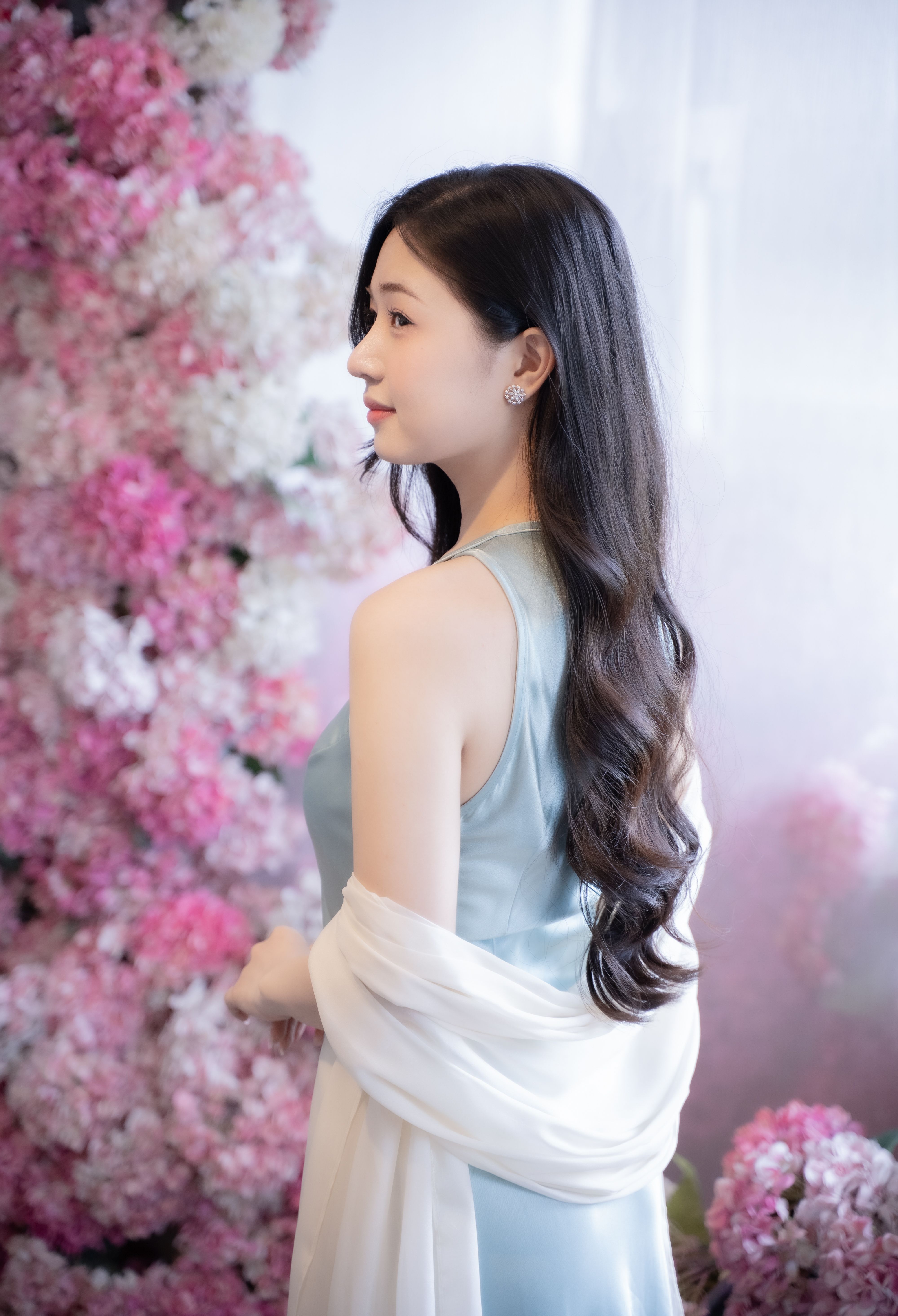 A woman in a blue dress poses gracefully among pink and white flowers, exuding elegance and charm.